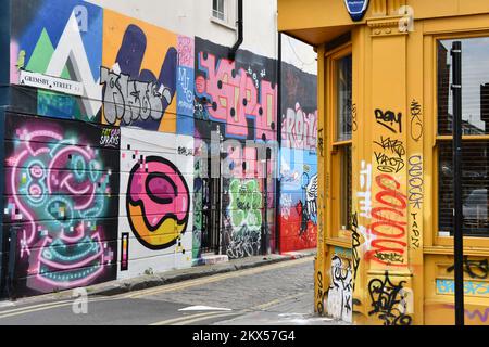 Graffiti e Street art parete coperta in Grimsby Street, Shoreditch, Londra, con un negozio giallo fronte coperto di graffiti Foto Stock