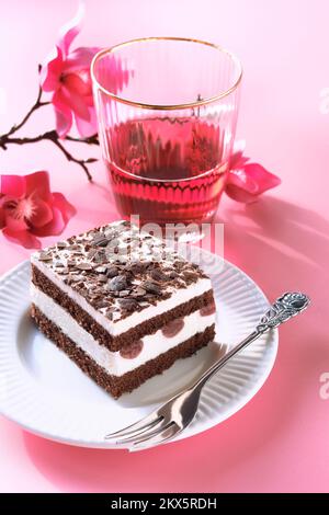 Torta al cioccolato con ciliegie acide. Pezzo di torta su un piatto con forchetta. Dolce su sfondo rosa con fiori di Primavera magnolia, fiore rosa Foto Stock