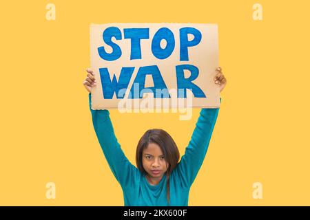 Ragazza che tiene il segno di guerra di arresto contro lo sfondo giallo. Slogan isolato di protesta della donna. Foto Stock