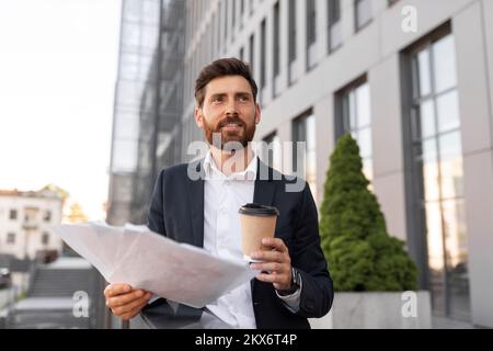 Giovane capo ragazzo europeo allegro e fiducioso con barba in vestito con documenti, gustare una tazza di drink da asporto Foto Stock