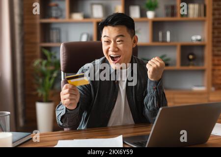 Soddisfatto sorpreso eccitato adulto giapponese uomo d'affari con la bocca aperta tenere carta di credito, fare il gesto di vittoria Foto Stock