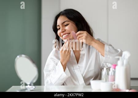 Donna araba felice che utilizza massaggiatore naturale, godendo di una pelle sana e luminosa Foto Stock