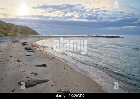 Tramonto sulla costa danese. Spiaggia, onde. Collina con alberi sullo sfondo. Foto di paesaggio dal mare Foto Stock