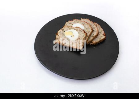 Piatto di festa rumeno chiamato Drobe, agnello tritato al forno o carne di maiale e fegato, con cipolla aglio prezzemolo e uova bollite al centro. fettine su un blac Foto Stock