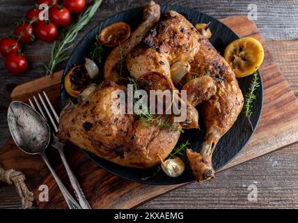 Cosce di pollo arrosto con limone, timo e aglio su tavolo di legno Foto Stock
