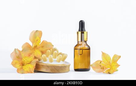 Bottiglia contagocce in vetro e spazzola e fiori in legno naturale per massaggi. Concetto - massaggio, cosmetologia, cosmesi, concetto di bellezza. Foto Stock