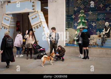 I membri del pubblico, compreso un proprietario dell'animale domestico che fotografa il suo cane, usano tutti i loro telefoni all'entrata del marchio di accessori di lusso, Louis Vuitton su Bond Street, il 30th novembre 2022, a Londra, Inghilterra. Foto Stock