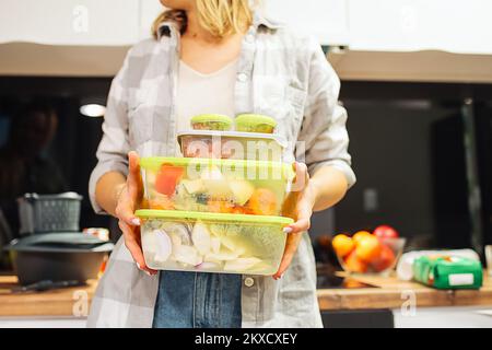 Le mani di una donna tengono contenitori di plastica con diversi alimenti congelati. Conservazione di alimenti ermeticamente sigillata. Cucina. Foto Stock