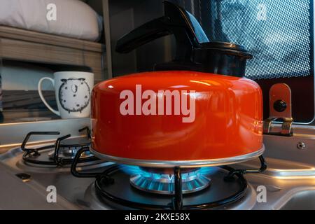 Un primo piano di un bollitore arancione fischiante su una stufa a gas in un camper con il gas acceso, Regno Unito Foto Stock