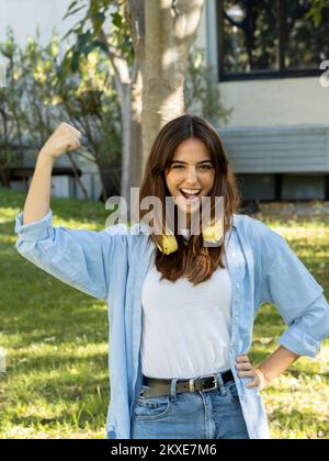 Giovane donna sorridente che guarda la macchina fotografica che mostra i bicipiti. Femminismo, empowerment femminile Foto Stock