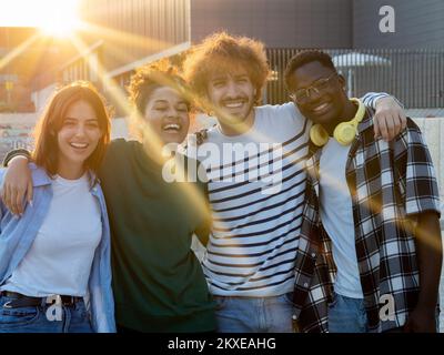 Gruppo di giovani amici multietnici che si sono godenti un bel momento durante un tramonto in città. Migliori amici Foto Stock