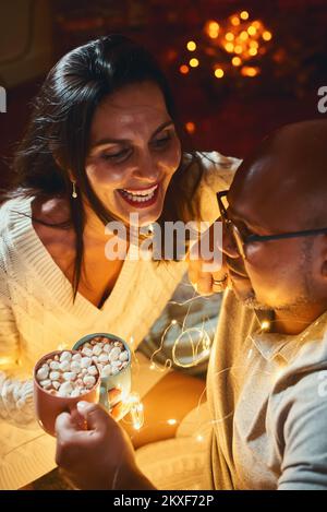 Felice coppia interracial che celebra il nuovo anno nel paese insieme che siede il garland vicino l'un l'altro Foto Stock