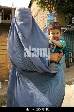 Kabul / Afghanistan: Donna vestita in un burqa blu che tiene un bambino. Foto Stock