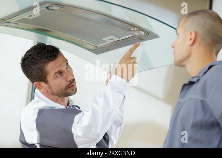 mentore e giovane uomo riparatore controllo filtro estrattore cucina Foto Stock