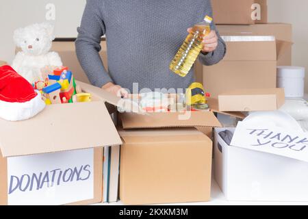 Donazioni natalizie per beneficenza. Volontario uomo che raccoglie cibo, vestiti, giocattoli per bambini, libri in scatole per donazioni. Donazione, beneficenza, banca di cibo, aiuto per Foto Stock