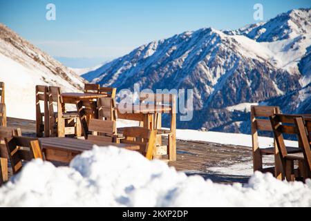 Terrazza ristorante all'aperto sulla cima di una montagna innevata con tavoli e sedie in legno. Foto Stock