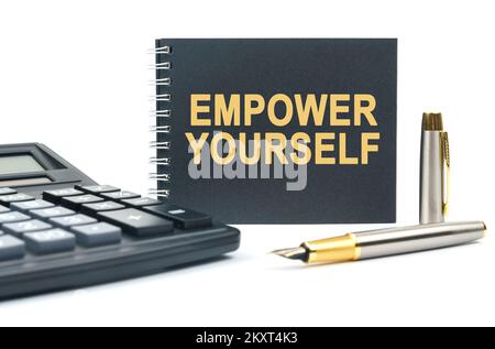Affari e finanza. Su uno sfondo bianco, c'è una calcolatrice, una penna e un notebook nero con l'iscrizione - EMPOWER TE STESSO Foto Stock