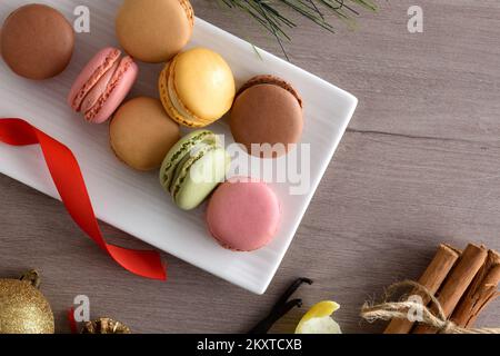 Macaroni francesi di vari sapori su un piatto bianco su tavola di legno con decorazioni natalizie e ingredienti. Vista dall'alto. Foto Stock