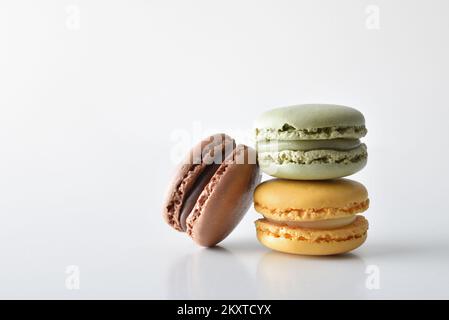 Pila di macarone francese a tre gusti, riflesso su un tavolo bianco e su uno sfondo bianco isolato. Vista frontale. Foto Stock