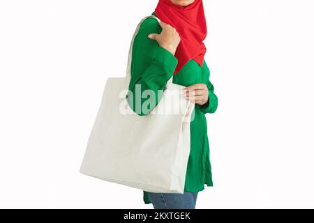 Primo piano di una donna musulmana che tiene in mano una borsa tote bianca bianca, che si sovrappone a uno sfondo bianco dello studio, uno spazio per le copie Foto Stock