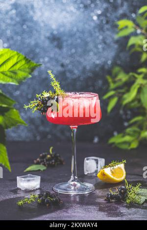 Elegante bicchiere di Gin Sour cocktail al ribes Nero o mocktail circondati da ingredienti sulla superficie scura del tavolo. Bevanda rinfrescante pronta per essere bevuta. Foto Stock