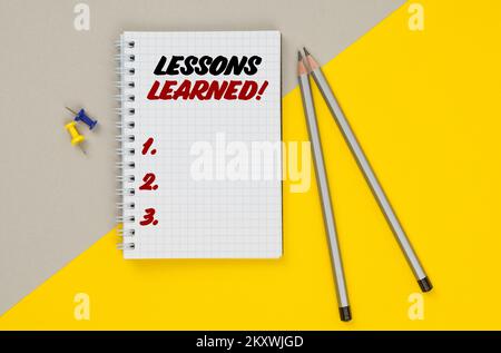 Affari e finanza. Su uno sfondo giallo-grigio ci sono matite, pulsanti e un notebook in cui è scritto - lezioni apprese Foto Stock