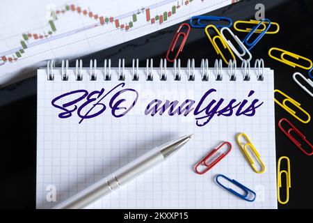Finanza ed economia. Sul desktop sono un grafico forex, clip di carta, una penna e un notebook in cui è scritto - analisi SEO Foto Stock