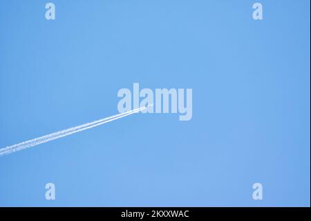 Aereo che vola attraverso un cielo blu chiaro lasciando un lungo sentiero dietro Foto Stock