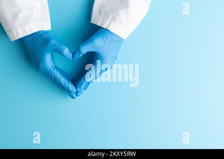 Le mani del medico indossando guanti medici che fanno la forma del cuore su sfondo blu Foto Stock