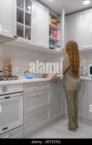 La giovane casalinga carina apre la porta dell'armadio della cucina Foto Stock