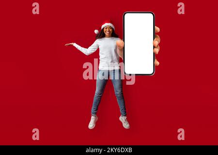 Felice bella donna nera in Santa Hat mostra smartphone, mockup Foto Stock