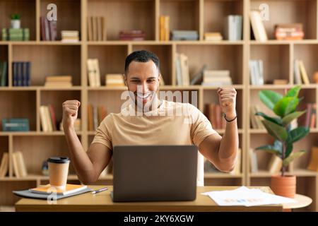 Successo aziendale. L'uomo arabo è stato molto contento di usare il notebook e di gesture sì, scuotendo i pugni per celebrare la grande fortuna Foto Stock