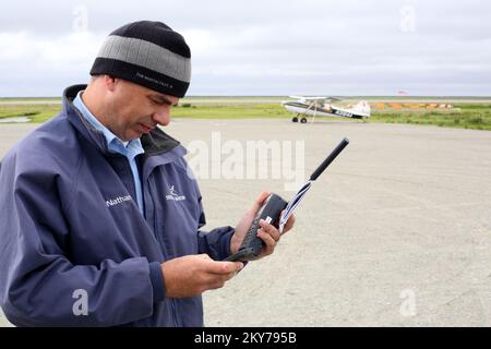 Alakanuk, Alaska, 16 luglio 2013 il pilota di sicurezza Nathan Semler chiama il controllo dei voli via telefono satellitare nel remoto territorio dello Yukon occidentale per ottenere la autorizzazione a decollare da questa pista di ghiaia. La FEMA sta rispondendo per l'invito del Governatore con le squadre a lavorare con lo Stato dell'Alaska e i sopravvissuti al disastro. Adam DuBrowa/ FEMA.. Fotografie relative a disastri e programmi, attività e funzionari di gestione delle emergenze Foto Stock