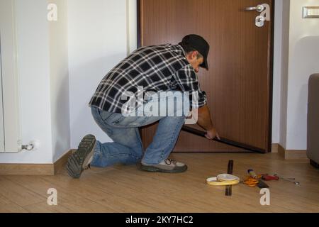 Immagine di un handyman che installa un dispositivo di esclusione della trazione sulla sua porta anteriore. Migliore isolamento termico e infiltrazione di aria fredda. Foto Stock