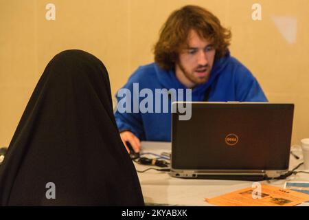 Dearborn, MI, 17 ottobre 2014 - David Andrew Chpernati (destra, giacca blu), FEMA Corps Silver 4 DSA Specialist, controlla il suo computer come egli aiuta un sopravvissuto al disastro registrarsi con FEMA in un Disaster Recovery Site (RSS) presso il Centro Islamico d'America a Dearborn, Michigan in risposta alle gravi tempeste e alluvioni del 11-13 agosto 2014 che hanno colpito negativamente le contee del Michigan di Wayne, Oakland e Macomb. La FEMA sostiene i governi locali e statali e le entità tribali nei loro sforzi per riprendersi dalle catastrofi naturali. Michigan forti tempeste e inondazioni. Fotografie relative al disgusto Foto Stock