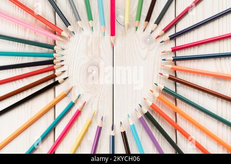 Composizione di matite colorate che formano la forma del cuore da matite di ardesia su fondo di legno bianco. San Valentino e carattino d'amore per Foto Stock