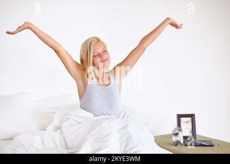 Sentirsi freschi e riposati. Una giovane donna attraente che si allunga a letto dopo il risveglio. Foto Stock