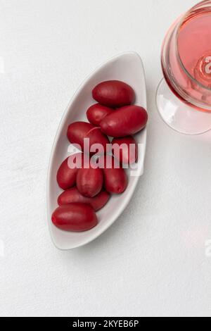 Olive rosse in una ciotola bianca, un bicchiere di vino rosso. Sfondo bianco. Spazio di copia. Giacitura piatta. Foto Stock