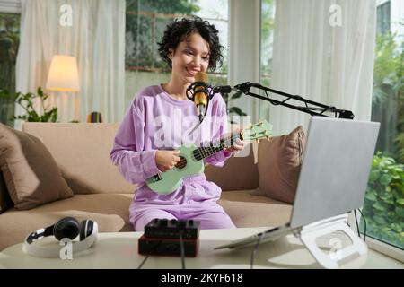 Ragazza giovane sorridente che canta in mike e che gioca ukulele Foto Stock