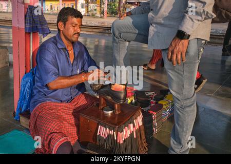 Un uomo polacco-wallah o shoeshine, un migrante da Bihar nell'India del Nord, lucidando la scarpa di un cliente alla stazione di Matunga a Mumbai, in India Foto Stock