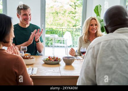 Due coppie mature diverse si sono riunite a tavola divertendosi Foto Stock