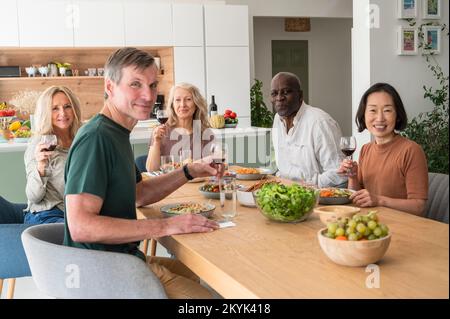 Gruppo di amici anziani diversi si sono riuniti per il pranzo in cucina Foto Stock