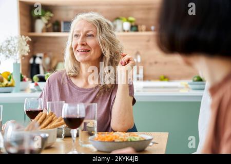 Foto di una donna matura seduta a tavola che si gode un pasto con gli amici Foto Stock