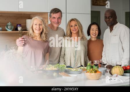 Ritratto di gruppo di diversi amici anziani in piedi a Kitchen Island dopo aver cucinato Foto Stock