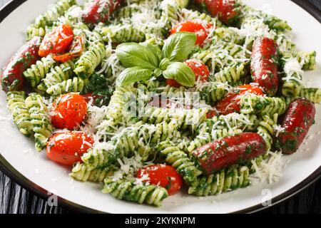 Insalata italiana di fusilli con salsicce, pomodori, pesto e parmigiano primo piano in un piatto sul tavolo. Orizzontale Foto Stock