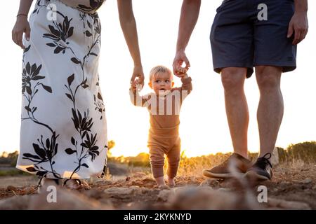 Bambina imparando a camminare con l'aiuto dei suoi genitori Foto Stock