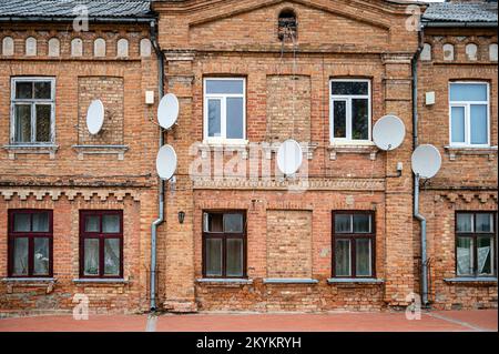 Molti piatti satellitari sulla facciata di un vecchio edificio in mattoni rossi, Bauska, Lettonia Foto Stock