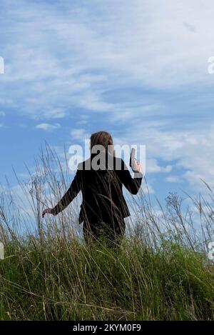 donna in tuta con pistola in piedi nel log grass. stile copertina libro a distanza media. Foto Stock