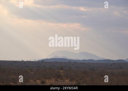 I raggi di luce solare si infrangono tra le nuvole sopra il parco nazionale di Ruaha nella stagione secca Foto Stock