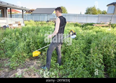 Giovane uomo con tosaerba a benzina che lavora sul suo cortile Foto Stock